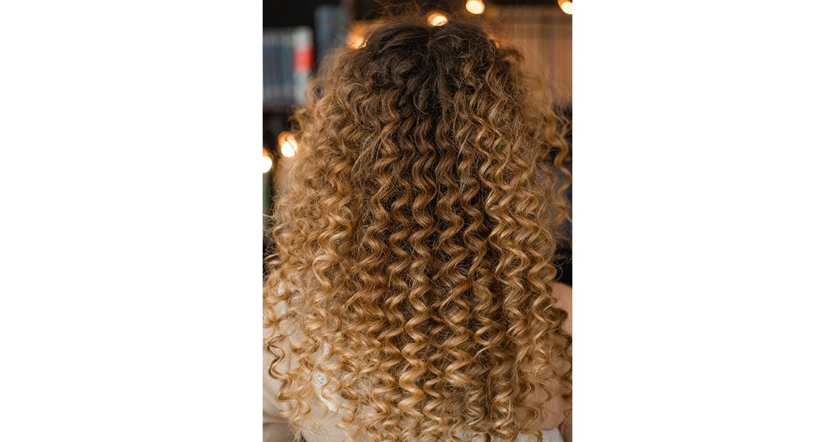 mulher com cabelo comprido cacheado em tons de loiro mel